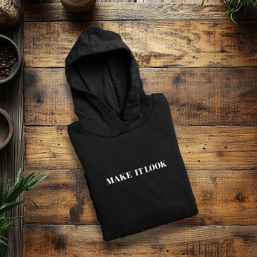 Zusammengelegter schwarzer Hoodie mit weißem Schriftzug auf einem Holztisch, daneben grüne Pflanzen